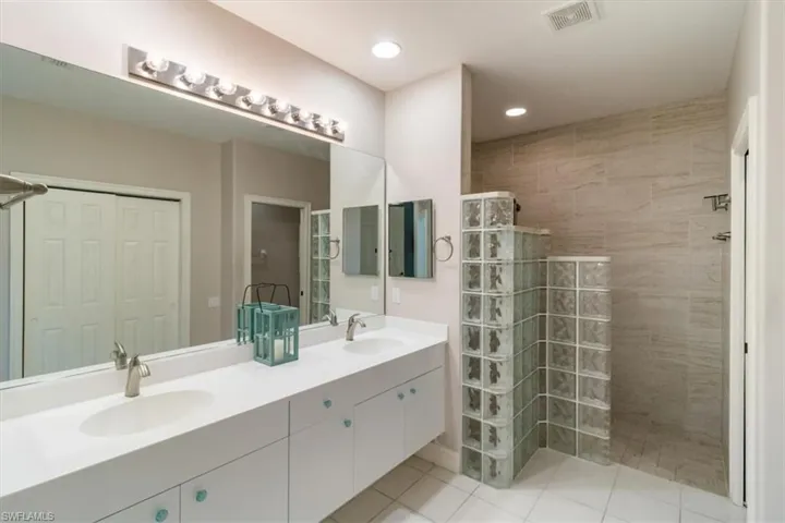 Bathroom with updated coastal tile shower, double sink, oversized vanity, and tile floors