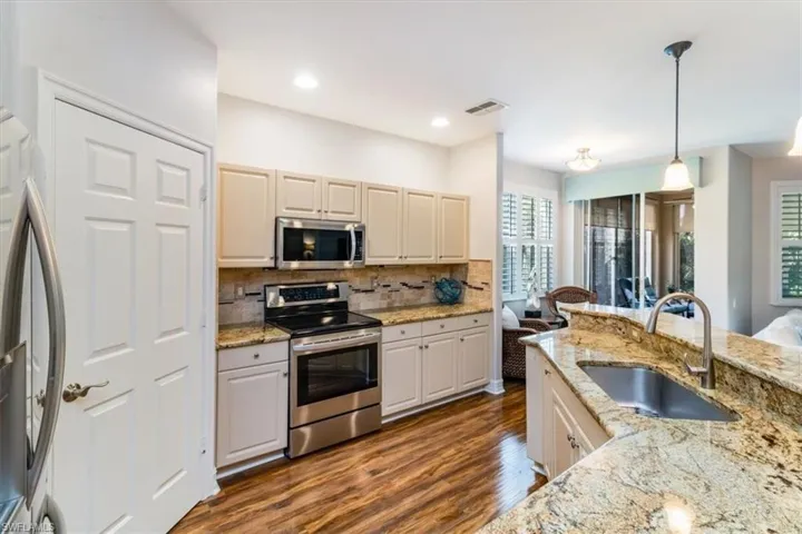 Kitchen featuring stainless steel appliances, backsplash, wood flooring, sink, and pendant lighting
