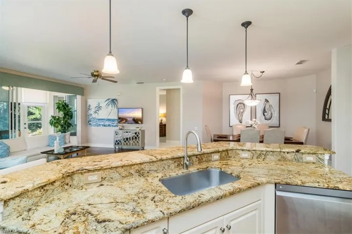 Kitchen featuring light stone countertops, hanging light fixtures, stainless steel dishwasher, white cabinets, and sink