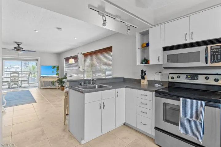 Kitchen with sink, appliances with stainless steel finishes, track lighting, white cabinets, and kitchen peninsula