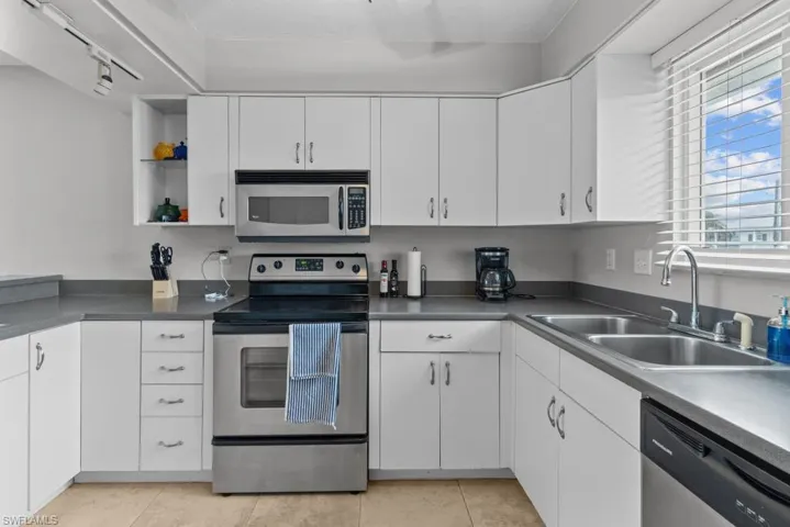 Kitchen with light tile patterned flooring, rail lighting, sink, white cabinetry, and stainless steel appliances