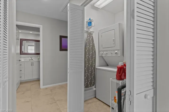 Laundry room with stacked washer and clothes dryer and light tile patterned floors