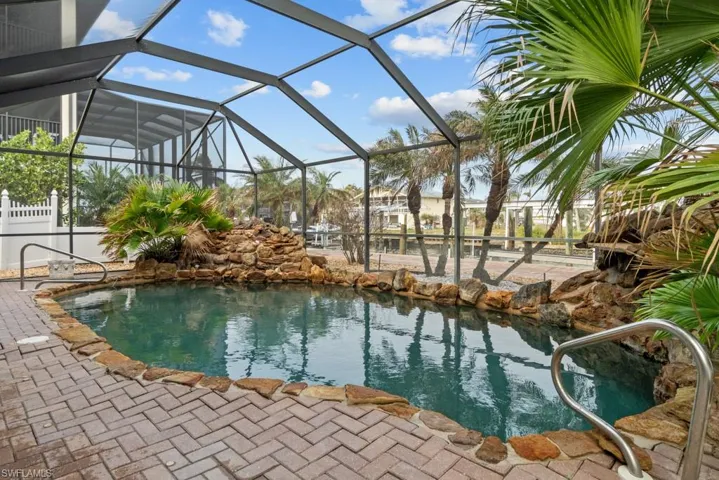 View of pool with a lanai and a small pond