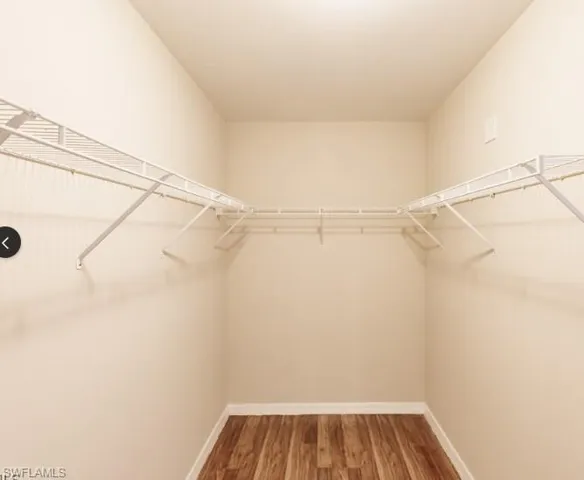Walk-in closet featuring light beige walls, white wire shelving, white baseboards, and wood-finish flooring