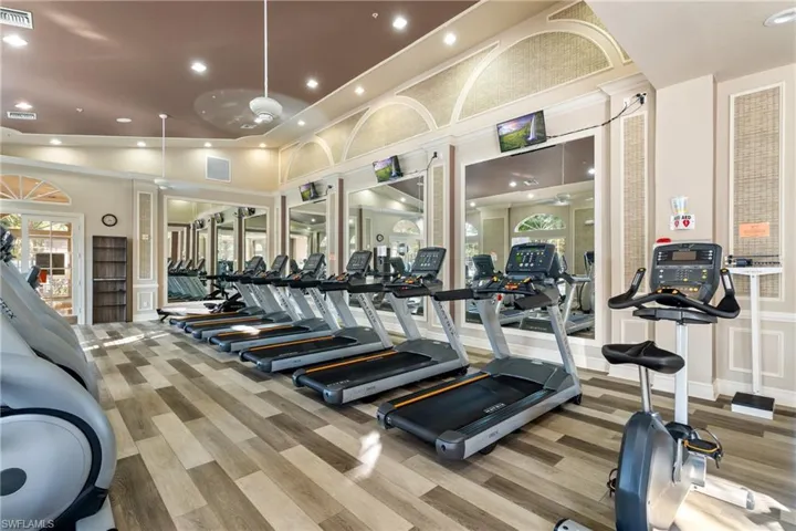 Exercise room featuring ceiling fan, light wood-type flooring, and lofted ceiling
