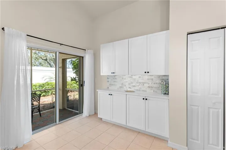 Kitchen with light tile patterned floors, white cabinets, high vaulted ceiling, and backsplash