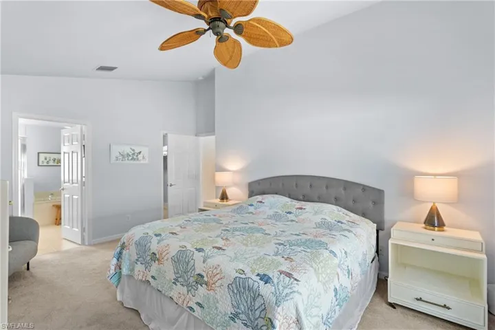Carpeted bedroom with vaulted ceiling, connected bathroom, and ceiling fan