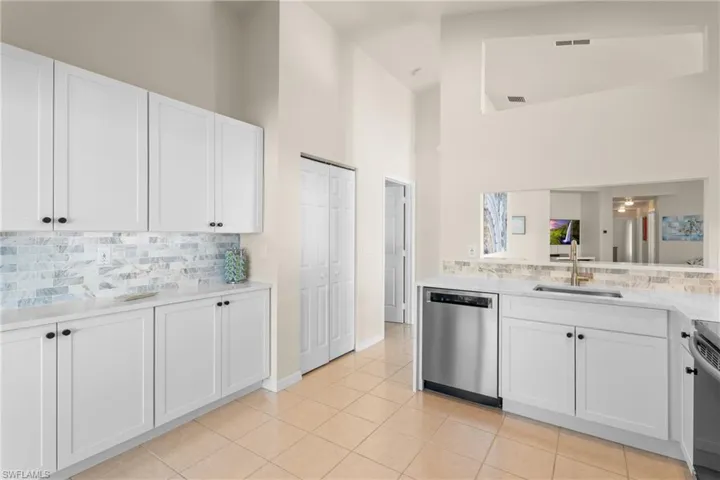 Kitchen featuring stainless steel dishwasher, light tile patterned flooring, white cabinetry, and sink