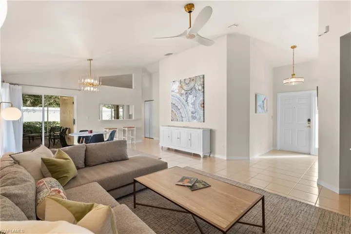 Living room featuring high vaulted ceiling, ceiling fan with notable chandelier, and light tile patterned floors