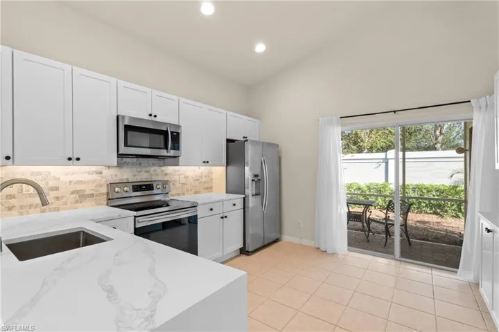 Kitchen featuring stainless steel appliances, sink, white cabinetry, light stone counters, and decorative backsplash