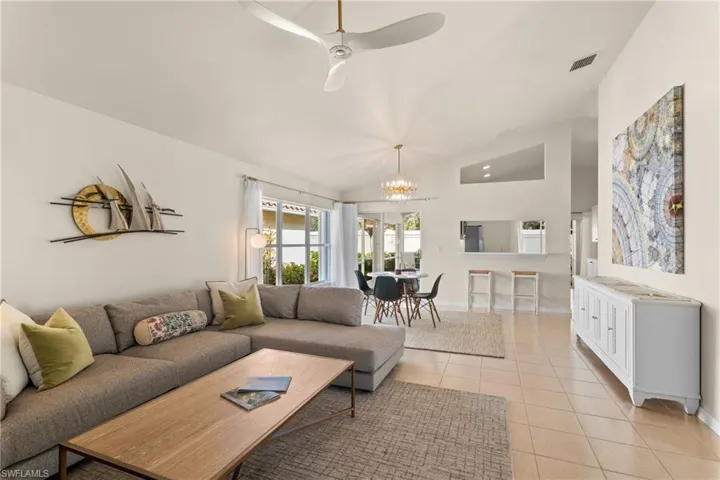 Living room featuring ceiling fan with notable chandelier, light tile patterned flooring, and vaulted ceiling
