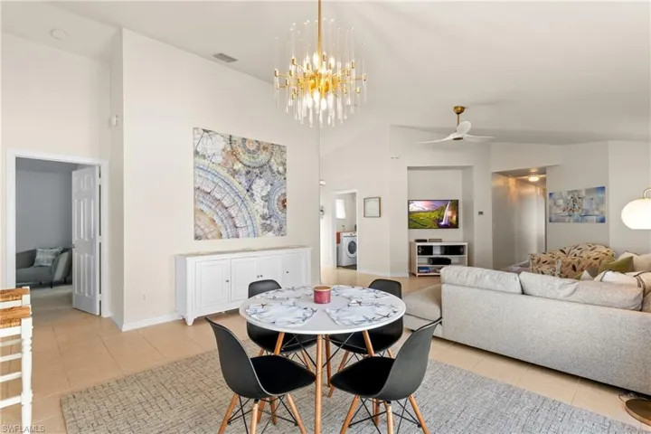 Tiled dining area featuring ceiling fan with notable chandelier, high vaulted ceiling, and washer / clothes dryer