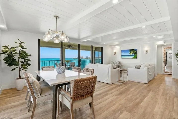 Open-concept living and dining area featuring wide-plank wood-finish flooring, a shiplap ceiling, and extensive floor-to-ceiling sliding glass doors opening to a covered balcony - Virtually Edited Image
