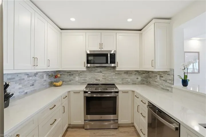 Kitchen featuring stainless steel appliances, light stone counters, white cabinets, recessed lighting, and light wood-style flooring - Virtually Edited Image