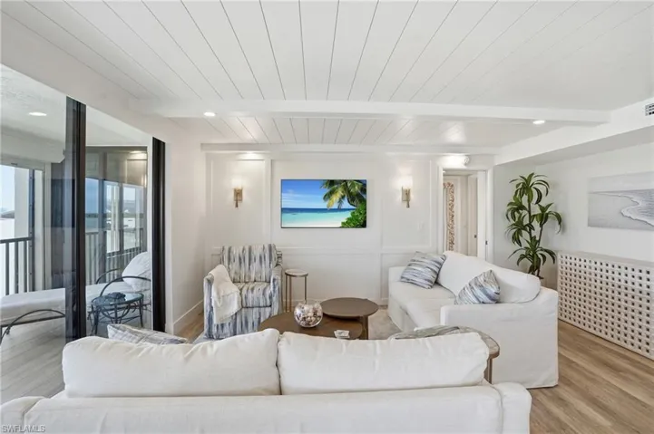 Living area with wood finished floors, a wood ceiling with exposed beams, and a decorative wall - Virtually Edited Image