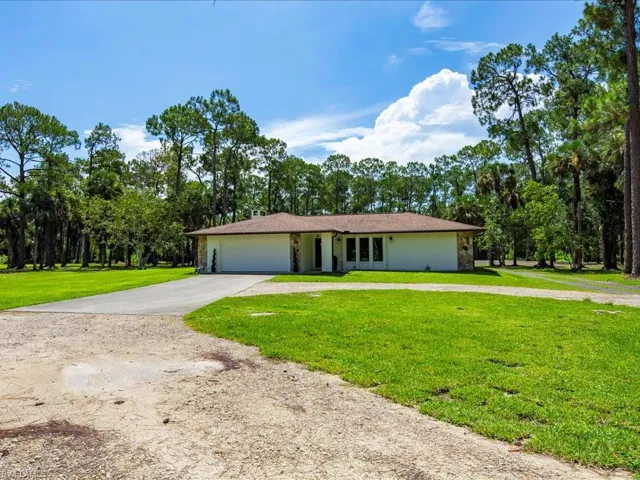 Ranch-style home featuring driveway, an attached garage, a front lawn, and view of wooded area