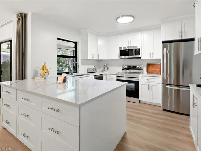 Kitchen featuring stainless steel appliances, white cabinetry, light stone countertops, and light wood-style flooring