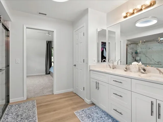 Bathroom featuring a marble finish shower, wood finished floors, double vanity, a walk in closet, and a ceiling fan