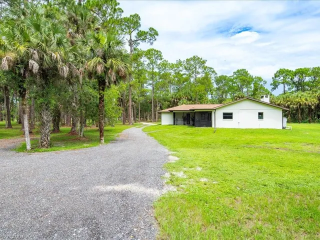 View of front of home with driveway, a front lawn, and view of wooded area