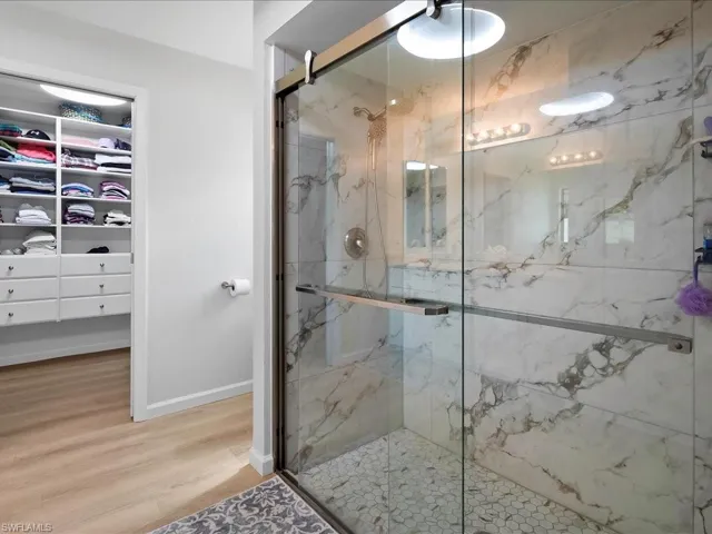 Full bathroom with a marble finish shower, a walk in closet, and wood finished floors