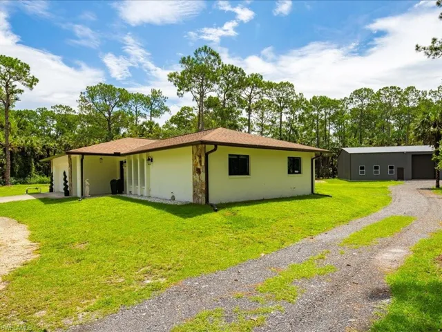 View of front of house featuring a front yard, driveway, stucco siding, and view of scattered trees