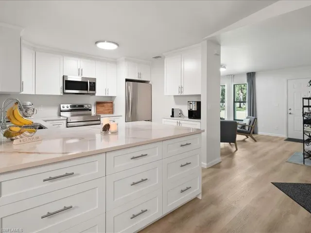 Kitchen featuring stainless steel appliances, light wood-style floors, white cabinets, a peninsula, and light stone counters