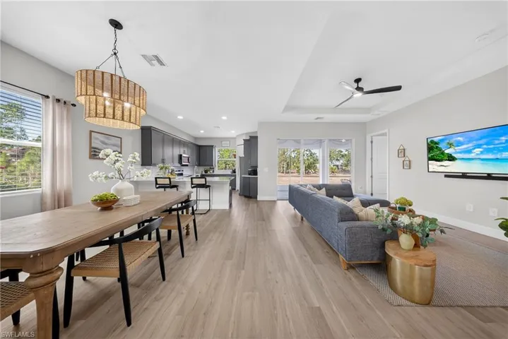 Living room featuring light wood-style flooring, ceiling fan, a raised ceiling, and recessed lighting