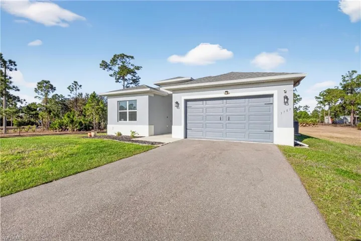 View of front facade featuring stucco siding, a front yard, driveway, and an attached garage