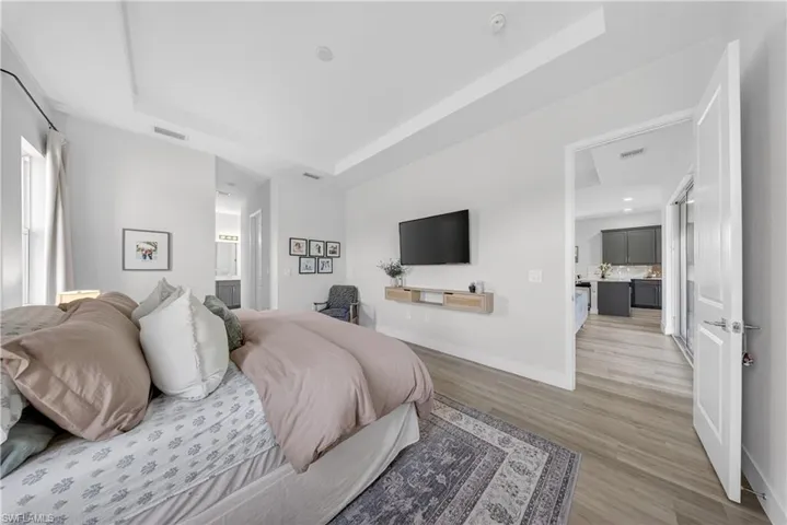 Bedroom with a tray ceiling, light wood-type flooring, and connected bathroom