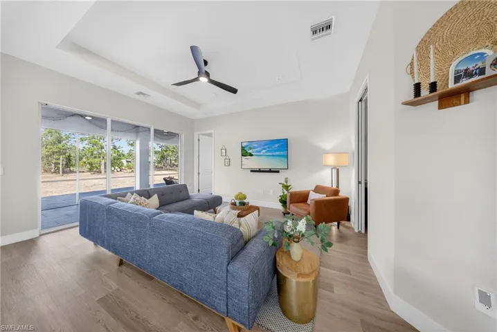 Living room featuring a tray ceiling, ceiling fan, and light wood-style flooring
