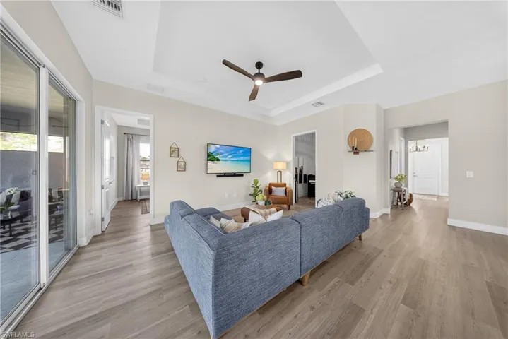 Living room with a ceiling fan, light wood-type flooring, and a raised ceiling