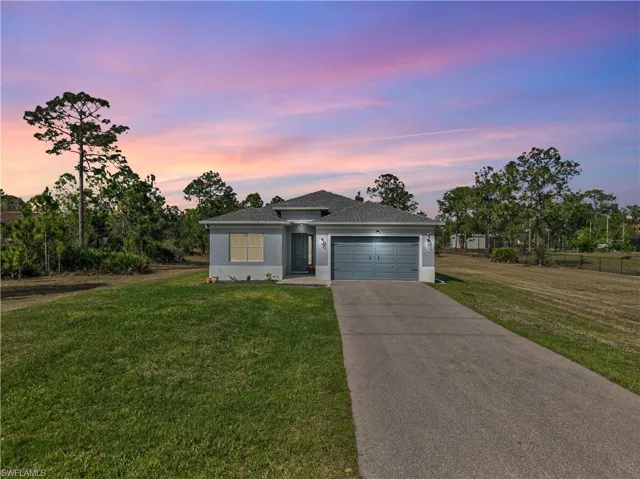 View of front of house featuring a front yard, an attached garage, driveway, roof with shingles, and stucco siding