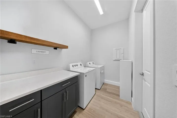 Laundry area featuring light wood finished floors, washing machine and dryer, vaulted ceiling, cabinet space, and a textured wall