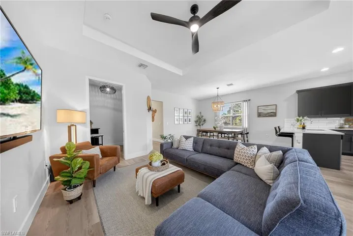 Living room with ceiling fan, light wood-type flooring, a tray ceiling, and recessed lighting