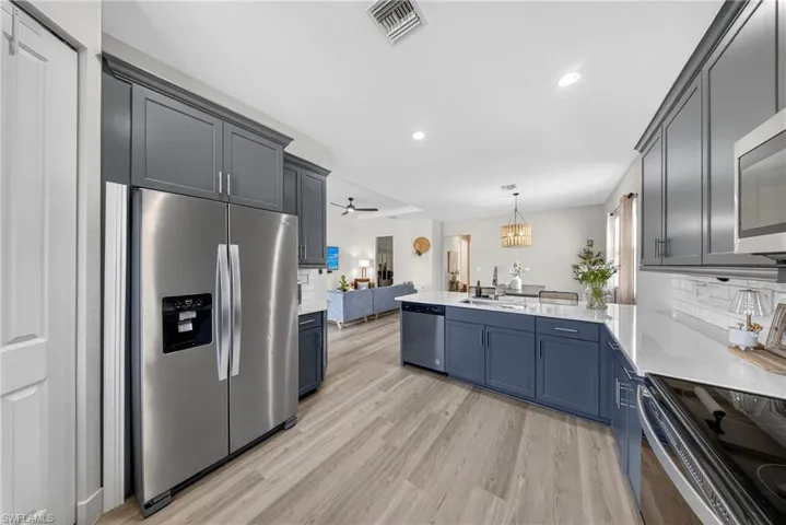 Kitchen with a peninsula, stainless steel appliances, open floor plan, light stone counters, and light wood finished floors