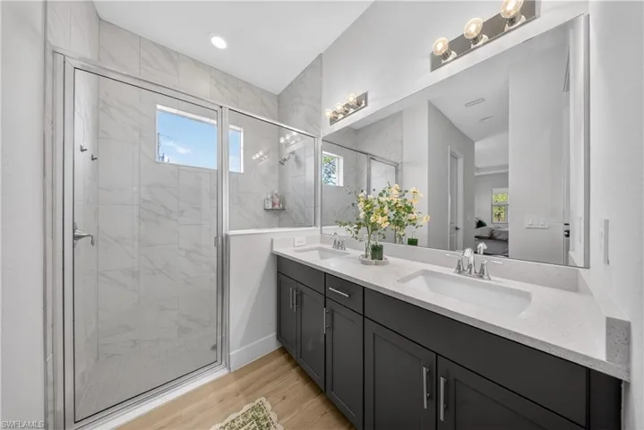 Ensuite bathroom featuring double vanity, a marble finish shower, light wood-style flooring, and recessed lighting