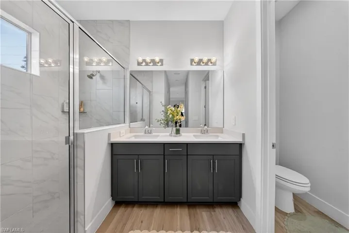 Full bath with double vanity, light wood finished floors, and a stall shower