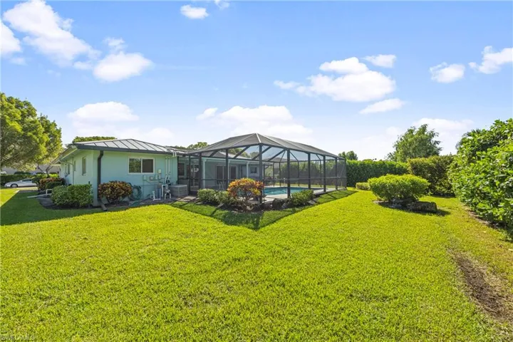 Rear view of property with a sunroom, glass enclosure, a lawn, a standing seam roof, and an outdoor pool