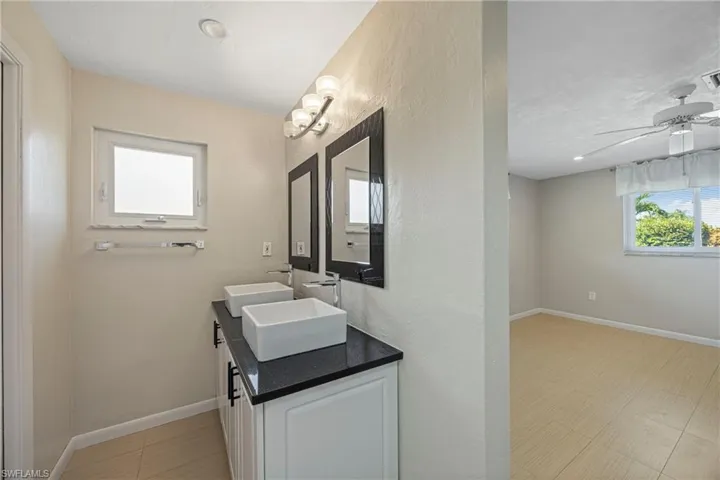 Full bath featuring double vanity, a textured wall, a ceiling fan, and light tile patterned flooring
