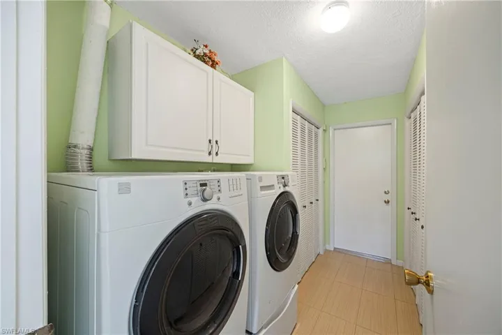 Laundry room featuring a textured ceiling, washing machine and dryer, cabinet space, and light tile patterned floors