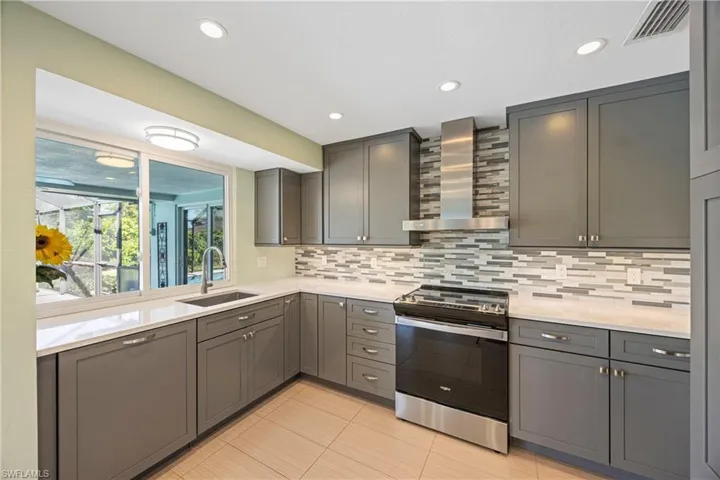 Kitchen with electric stove, wall chimney exhaust hood, recessed lighting, backsplash, and light stone counters