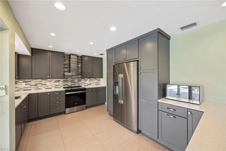 Kitchen featuring stainless steel appliances, light stone counters, wall chimney range hood, tasteful backsplash, and recessed lighting