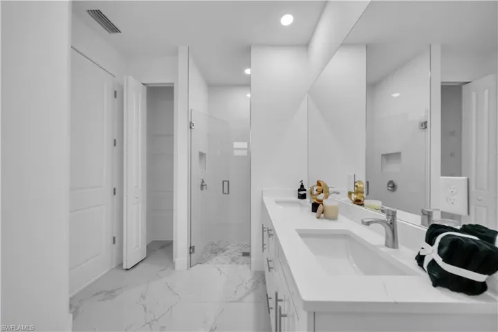 Full bath with a shower stall, double vanity, recessed lighting, and light marble finish floors