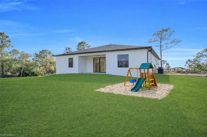 Rear view of house with a playground, a lawn, a patio area, and stucco siding