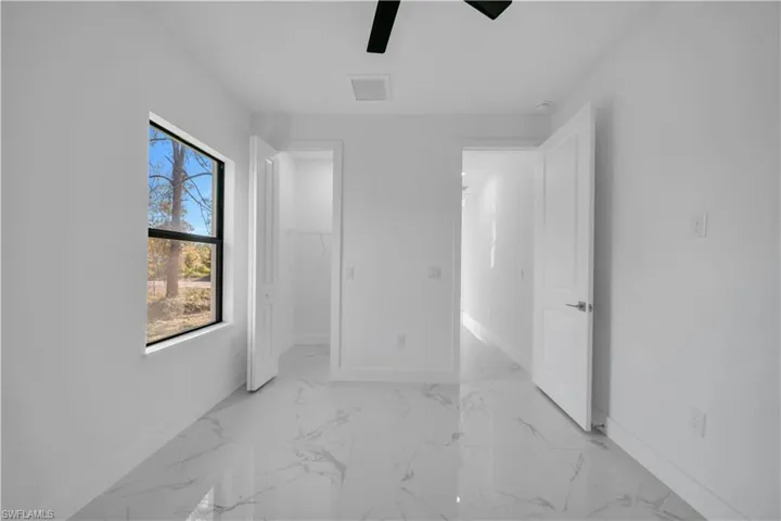 Unfurnished bedroom featuring a walk in closet, light marble finish floors, and ceiling fan