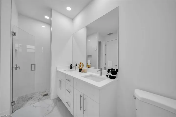 Bathroom featuring double vanity, a shower stall, light marble finish flooring, and recessed lighting