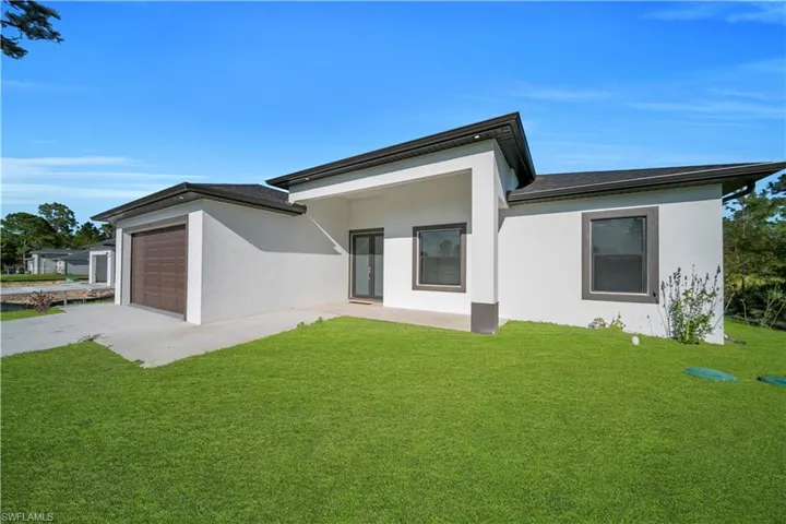 View of front facade featuring a front lawn, concrete driveway, stucco siding, and a garage
