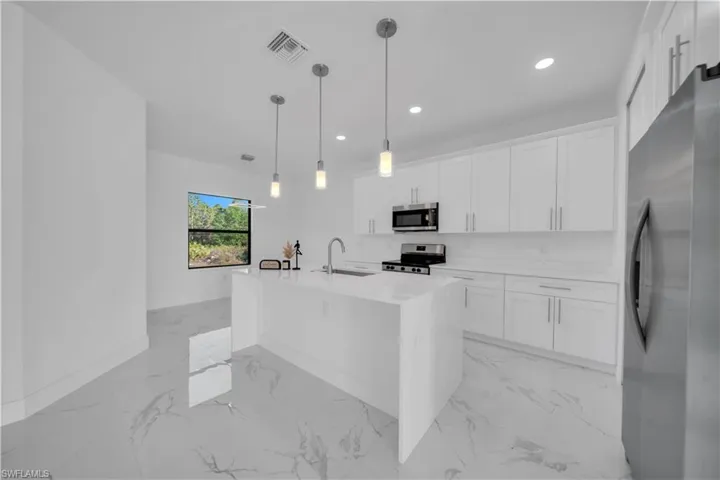 Kitchen with stainless steel appliances, light marble finish floors, white cabinetry, and light stone counters