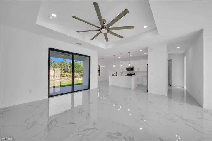 Unfurnished living room featuring a ceiling fan, recessed lighting, a tray ceiling, and light marble finish floors