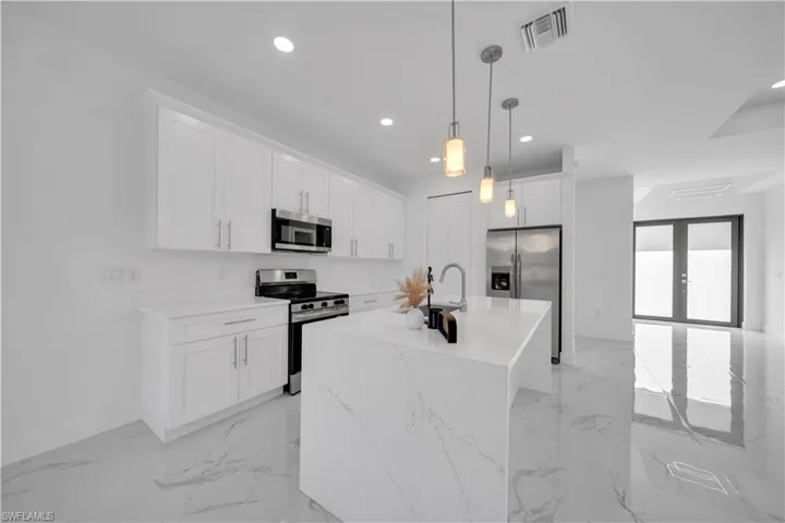 Kitchen with stainless steel appliances, light marble finish floors, white cabinetry, and an island with sink